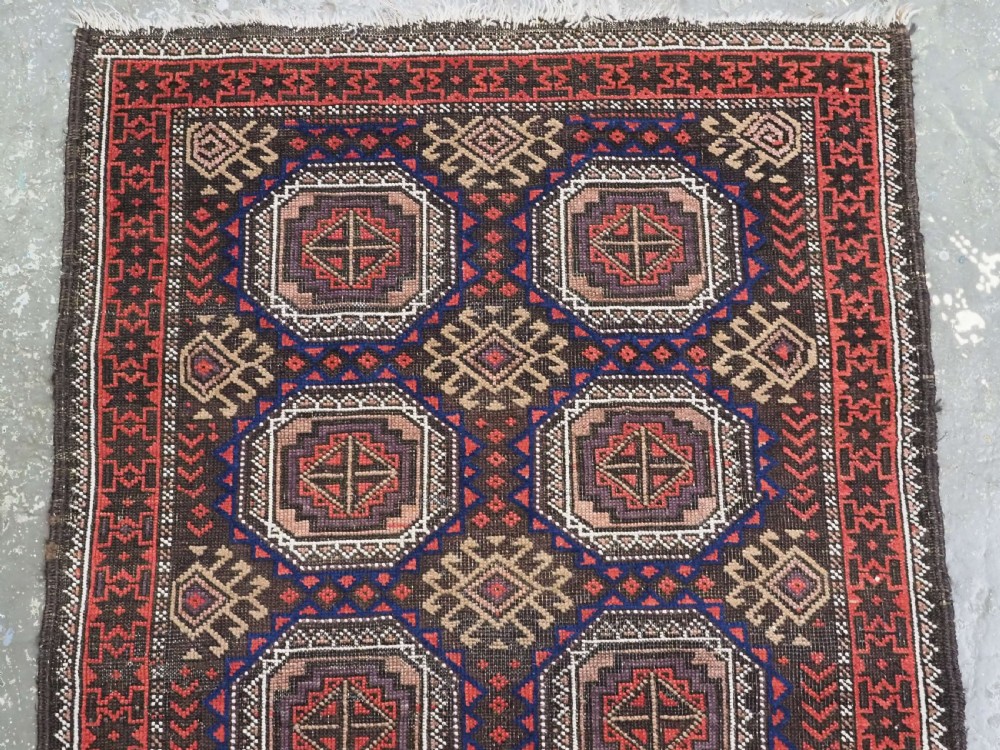 An antique hand-knotted Salar Khani Baluch wool rug featuring a central column of octagonal geometric medallions framed by intricate patterned borders in dark brown, deep red, and navy blue tones. View III