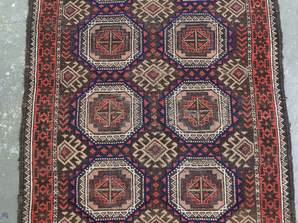 An antique hand-knotted Salar Khani Baluch wool rug featuring a central column of octagonal geometric medallions framed by intricate patterned borders in dark brown, deep red, and navy blue tones. View IV