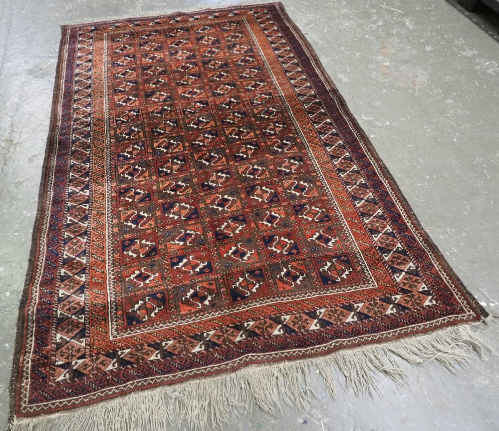 A rectangular hand-knotted antique Baluch rug featuring a grid of geometric motifs framed by decorative borders in terracotta, dark blue, and cream. View II