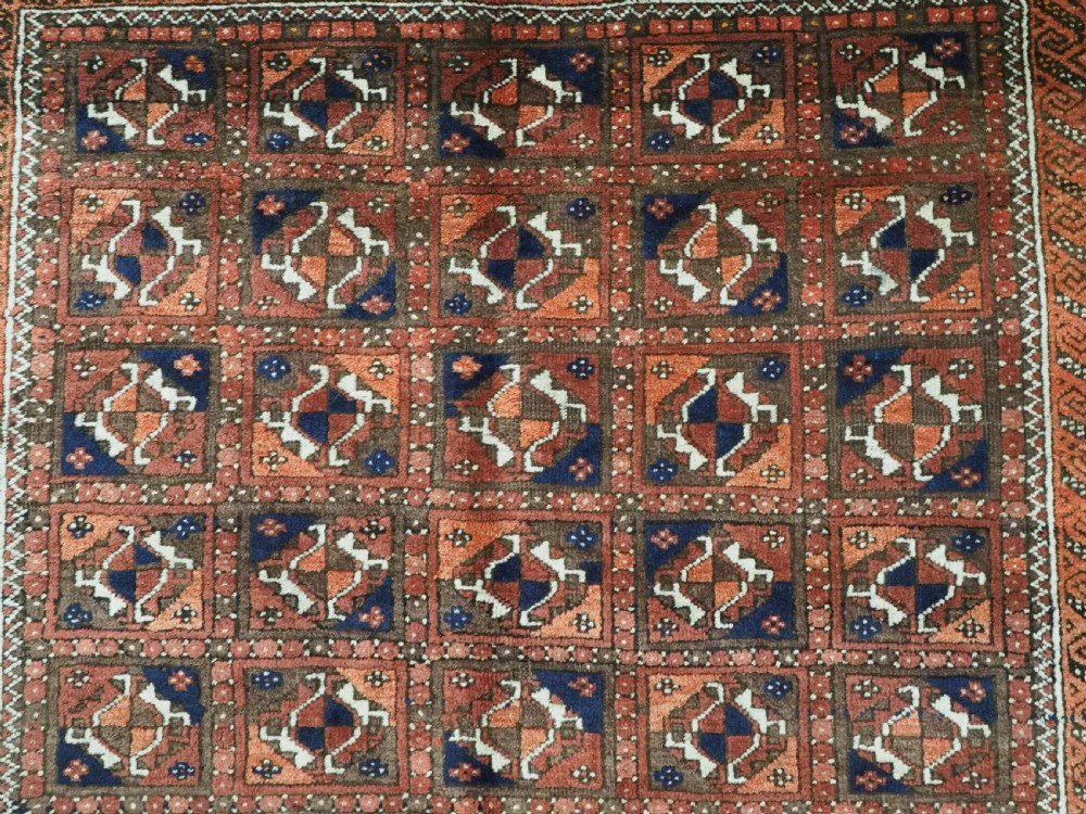 A rectangular hand-knotted antique Baluch rug featuring a grid of geometric motifs framed by decorative borders in terracotta, dark blue, and cream. View VIII