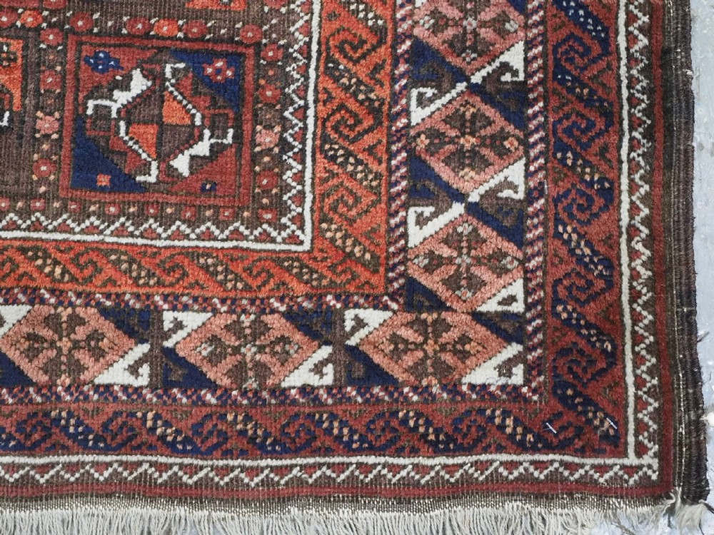 A rectangular hand-knotted antique Baluch rug featuring a grid of geometric motifs framed by decorative borders in terracotta, dark blue, and cream. View X