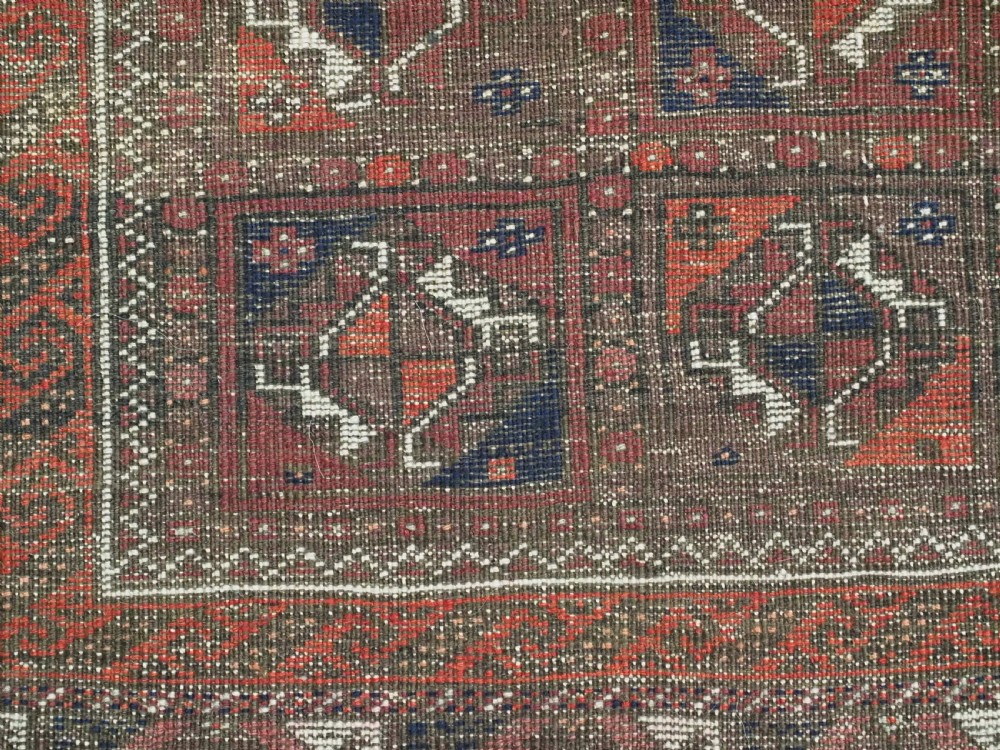 A rectangular hand-knotted antique Baluch rug featuring a grid of geometric motifs framed by decorative borders in terracotta, dark blue, and cream. View XI