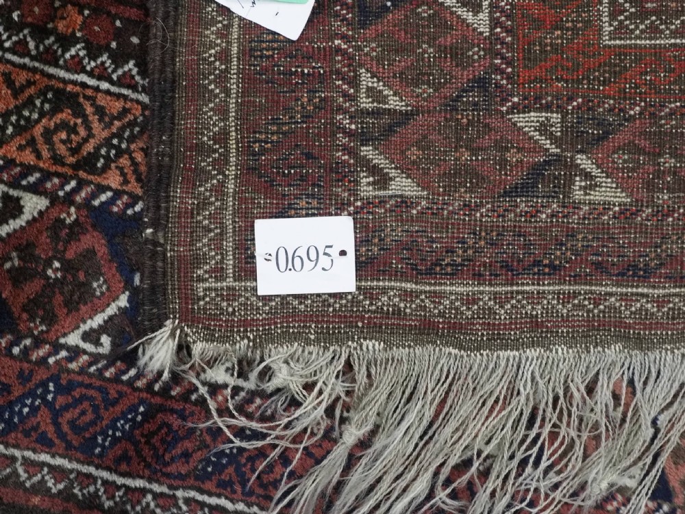 A rectangular hand-knotted antique Baluch rug featuring a grid of geometric motifs framed by decorative borders in terracotta, dark blue, and cream. View XII