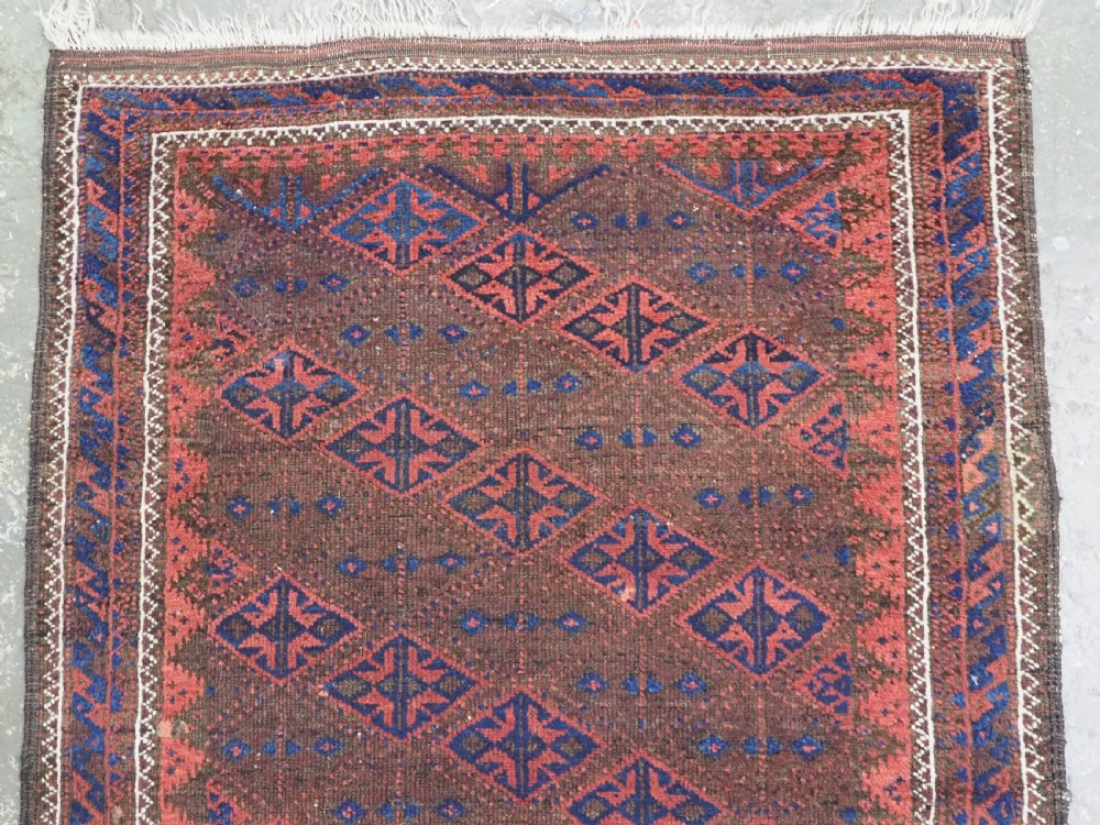 An antique Timuri Baluch hand-knotted wool rug with a dark brown field, repeating indigo and terracotta diamond motifs, and geometric borders. View III