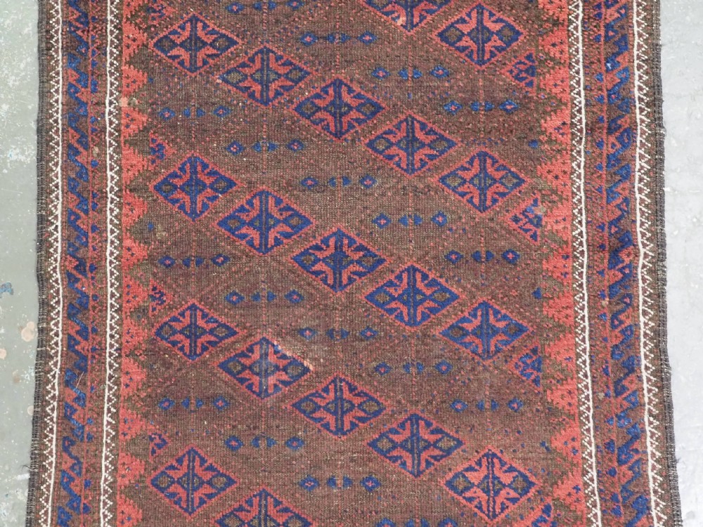 An antique Timuri Baluch hand-knotted wool rug with a dark brown field, repeating indigo and terracotta diamond motifs, and geometric borders. View IV