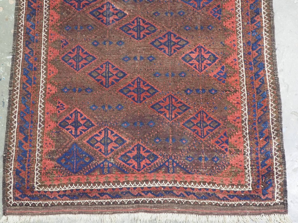 An antique Timuri Baluch hand-knotted wool rug with a dark brown field, repeating indigo and terracotta diamond motifs, and geometric borders. View V