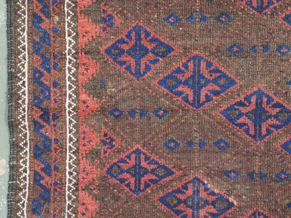 An antique Timuri Baluch hand-knotted wool rug with a dark brown field, repeating indigo and terracotta diamond motifs, and geometric borders. View VII