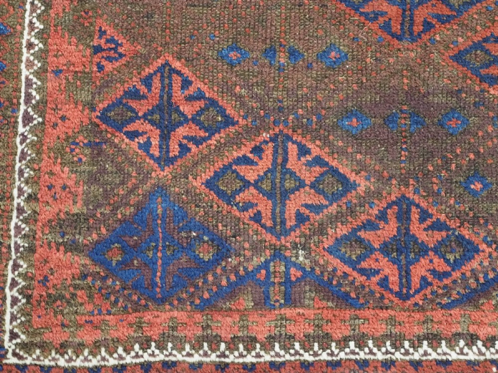 An antique Timuri Baluch hand-knotted wool rug with a dark brown field, repeating indigo and terracotta diamond motifs, and geometric borders. View IX