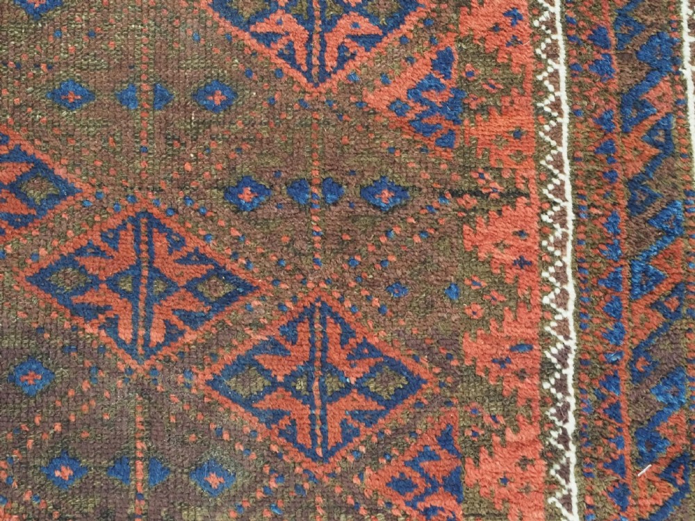 An antique Timuri Baluch hand-knotted wool rug with a dark brown field, repeating indigo and terracotta diamond motifs, and geometric borders. View X
