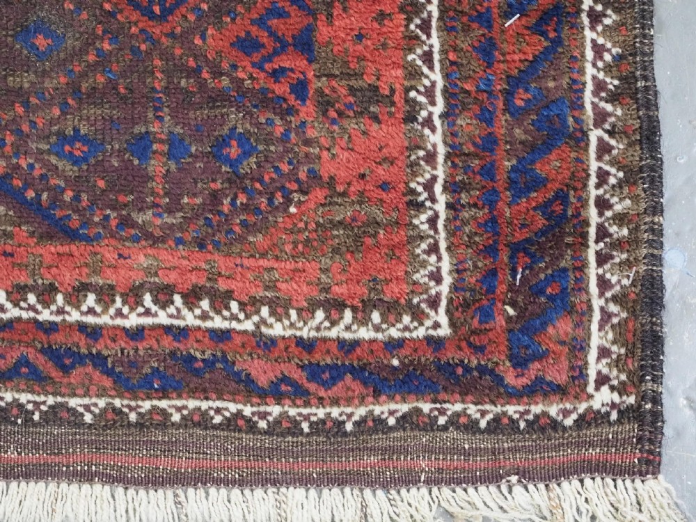 An antique Timuri Baluch hand-knotted wool rug with a dark brown field, repeating indigo and terracotta diamond motifs, and geometric borders. View XI