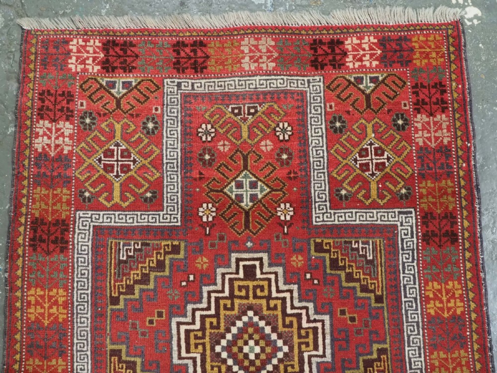 An antique hand-knotted Taimani Baluch prayer rug featuring a deep red field decorated with stepped geometric diamond motifs, a mihrab arch, and stylized geometric borders. View III