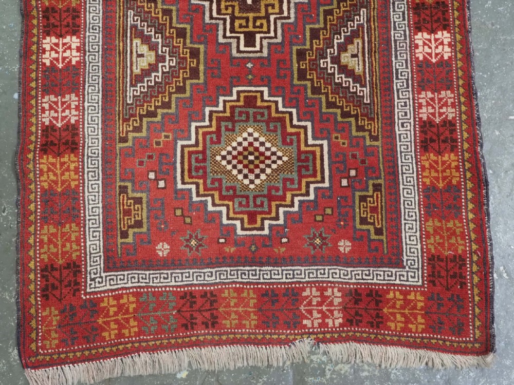An antique hand-knotted Taimani Baluch prayer rug featuring a deep red field decorated with stepped geometric diamond motifs, a mihrab arch, and stylized geometric borders. View V
