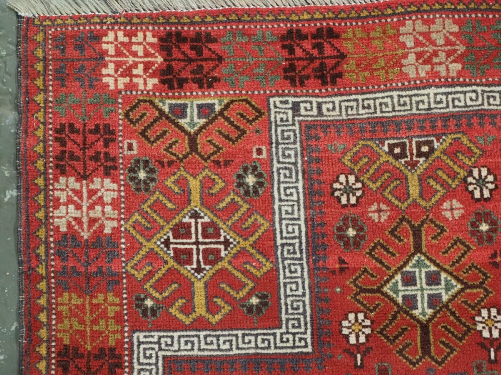 An antique hand-knotted Taimani Baluch prayer rug featuring a deep red field decorated with stepped geometric diamond motifs, a mihrab arch, and stylized geometric borders. View VII