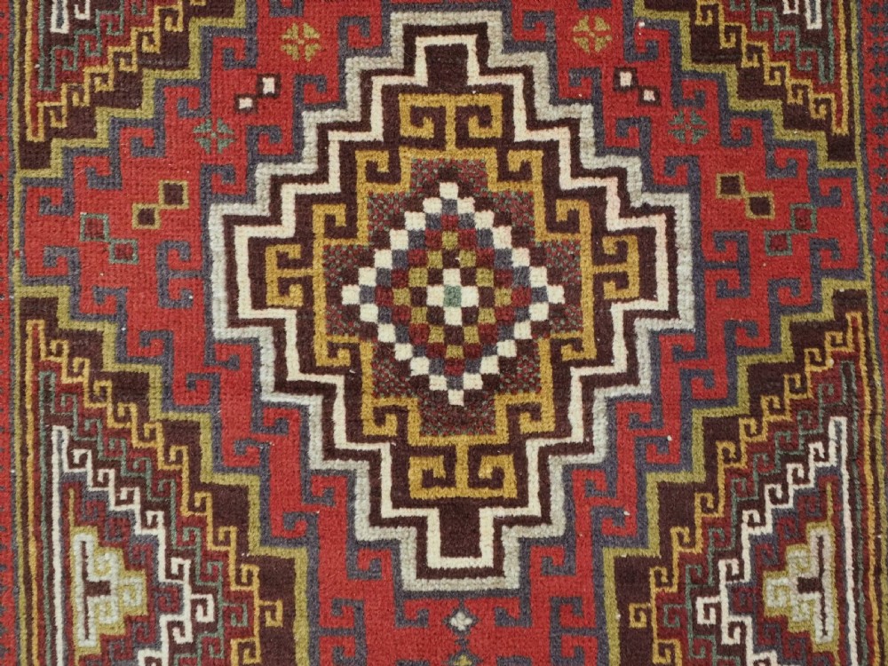 An antique hand-knotted Taimani Baluch prayer rug featuring a deep red field decorated with stepped geometric diamond motifs, a mihrab arch, and stylized geometric borders. View IX