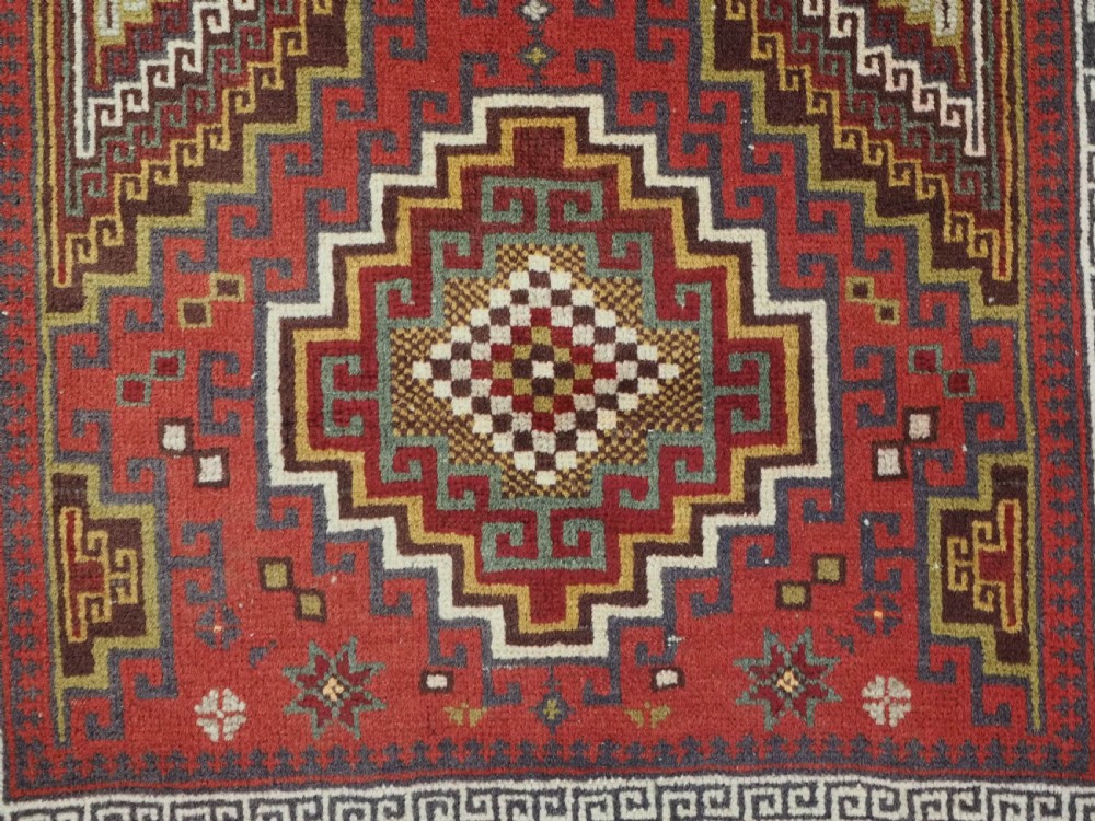 An antique hand-knotted Taimani Baluch prayer rug featuring a deep red field decorated with stepped geometric diamond motifs, a mihrab arch, and stylized geometric borders. View X