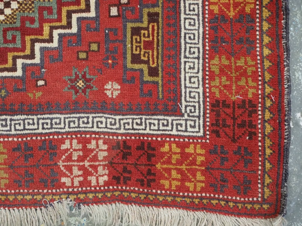 An antique hand-knotted Taimani Baluch prayer rug featuring a deep red field decorated with stepped geometric diamond motifs, a mihrab arch, and stylized geometric borders. View XI