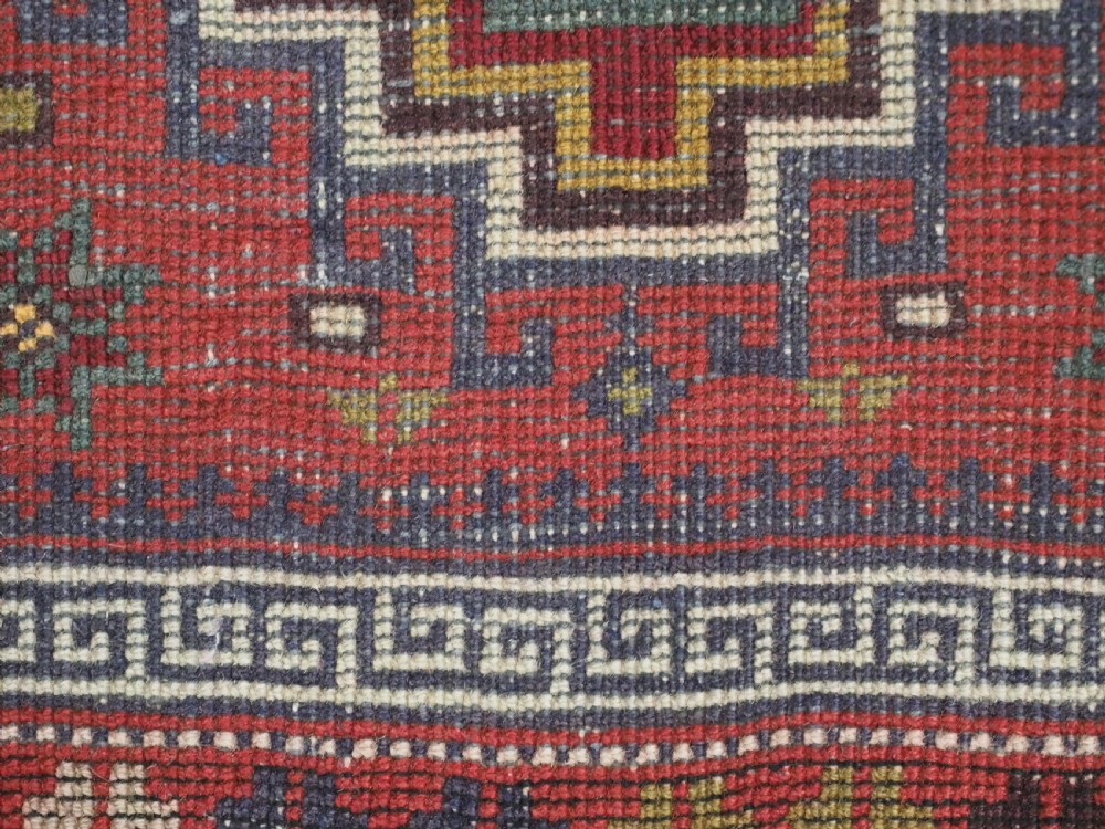 An antique hand-knotted Taimani Baluch prayer rug featuring a deep red field decorated with stepped geometric diamond motifs, a mihrab arch, and stylized geometric borders. View XII