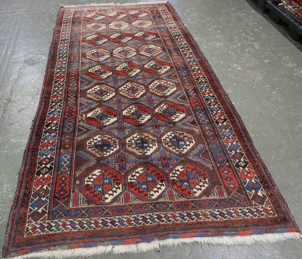 An antique long hand-knotted wool rug featuring geometric octagonal gul motifs in dark brown, red, blue, and cream tones. View II