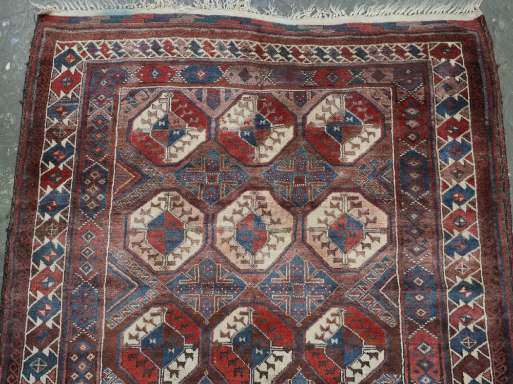 An antique long hand-knotted wool rug featuring geometric octagonal gul motifs in dark brown, red, blue, and cream tones. View III