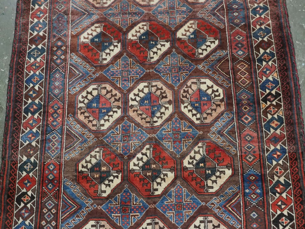 An antique long hand-knotted wool rug featuring geometric octagonal gul motifs in dark brown, red, blue, and cream tones. View IV