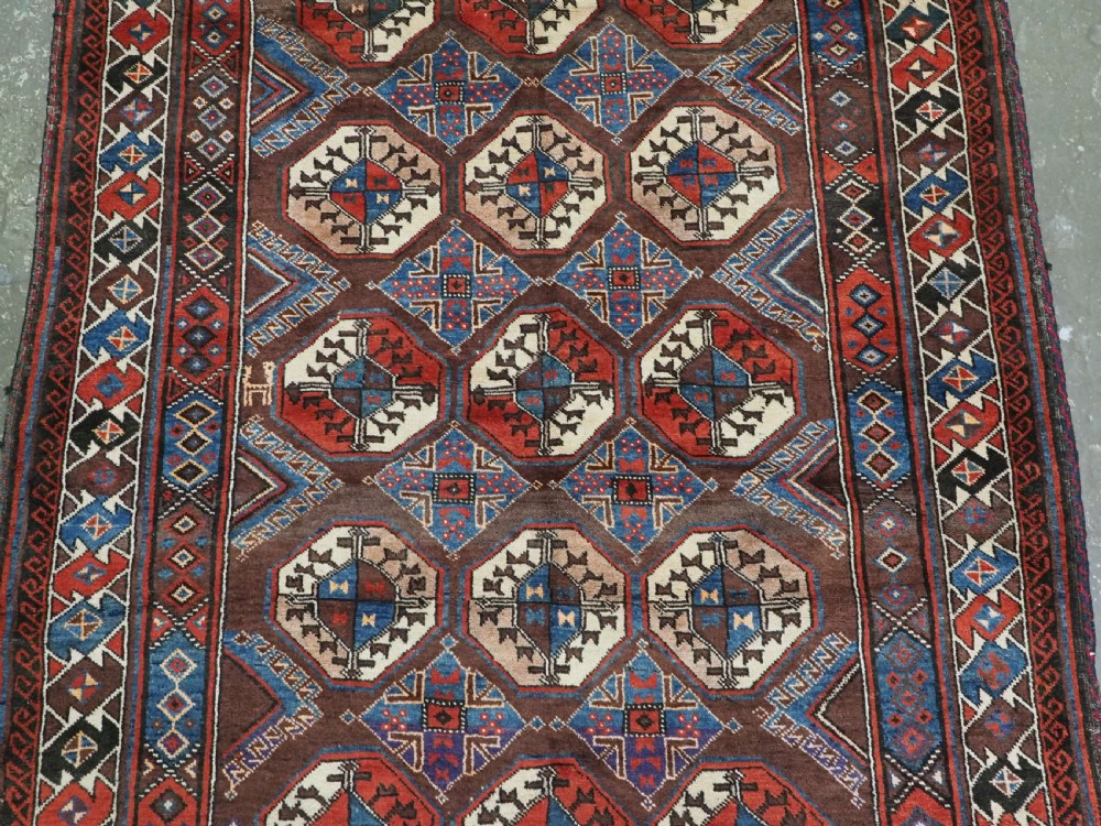 An antique long hand-knotted wool rug featuring geometric octagonal gul motifs in dark brown, red, blue, and cream tones. View V