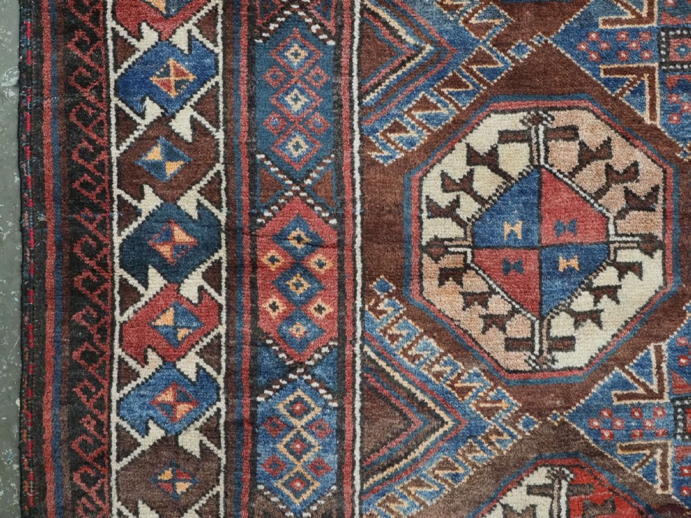 An antique long hand-knotted wool rug featuring geometric octagonal gul motifs in dark brown, red, blue, and cream tones. View VIII