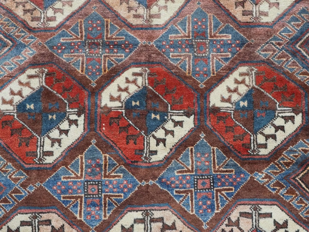 An antique long hand-knotted wool rug featuring geometric octagonal gul motifs in dark brown, red, blue, and cream tones. View IX