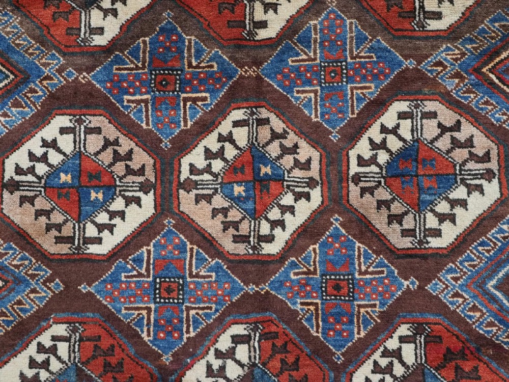 An antique long hand-knotted wool rug featuring geometric octagonal gul motifs in dark brown, red, blue, and cream tones. View X