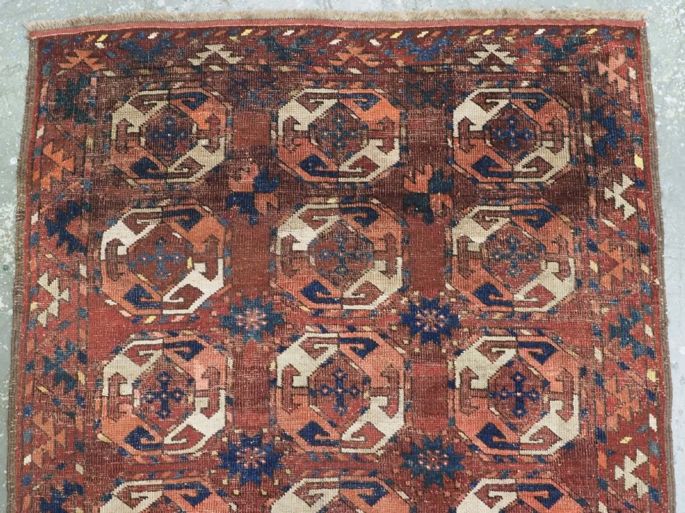 An antique woven wool rug featuring repeated octagonal gol motifs in cream, navy, and terracotta against a rich reddish-brown ground. View III