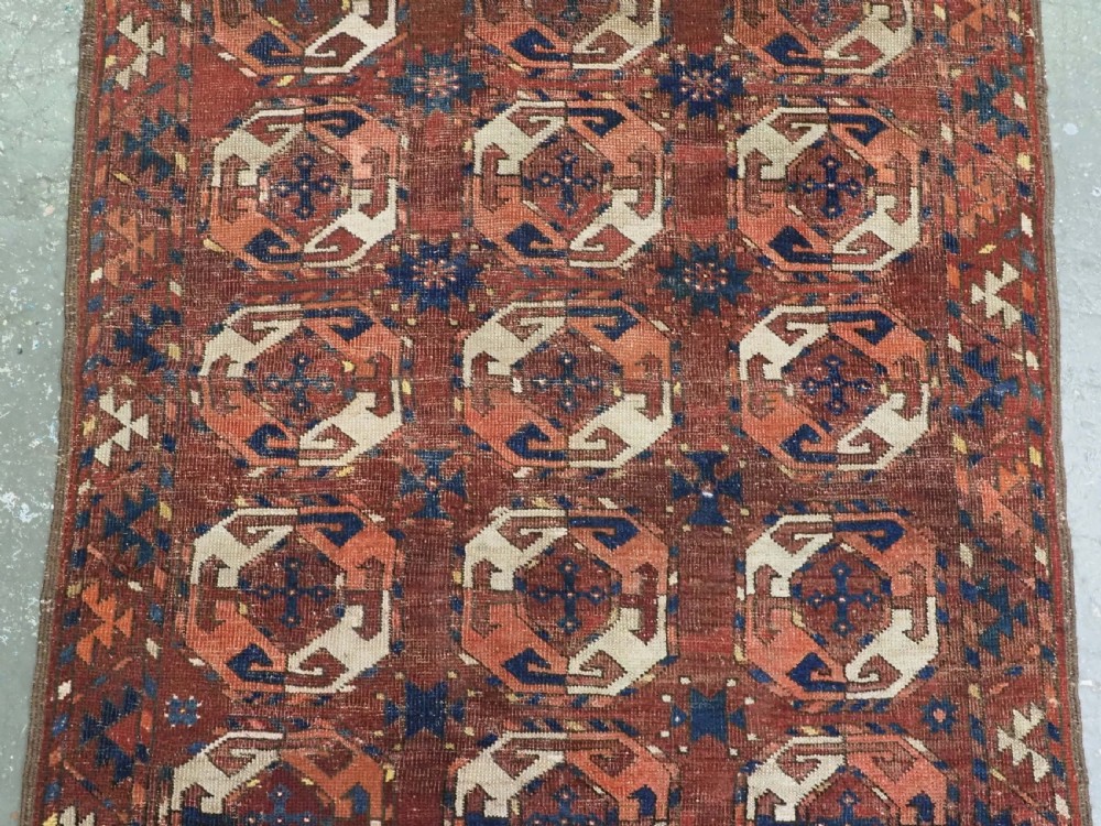 An antique woven wool rug featuring repeated octagonal gol motifs in cream, navy, and terracotta against a rich reddish-brown ground. View IV