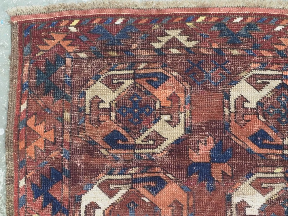 An antique woven wool rug featuring repeated octagonal gol motifs in cream, navy, and terracotta against a rich reddish-brown ground. View V