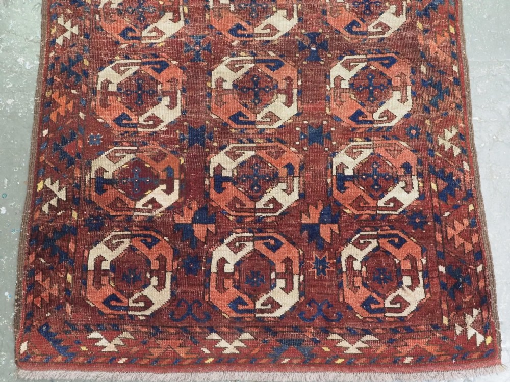 An antique woven wool rug featuring repeated octagonal gol motifs in cream, navy, and terracotta against a rich reddish-brown ground. View VI