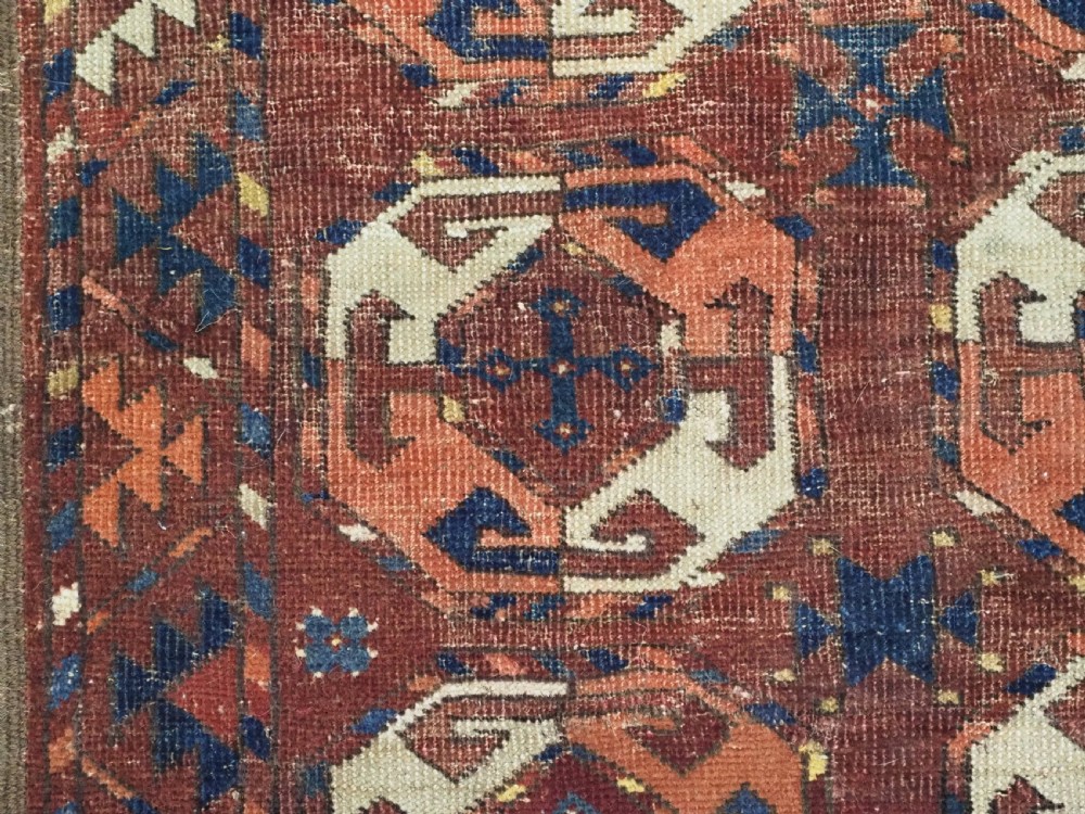 An antique woven wool rug featuring repeated octagonal gol motifs in cream, navy, and terracotta against a rich reddish-brown ground. View VII