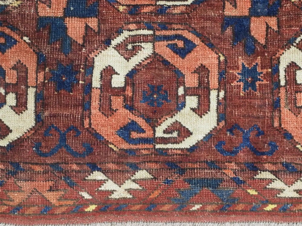 An antique woven wool rug featuring repeated octagonal gol motifs in cream, navy, and terracotta against a rich reddish-brown ground. View X