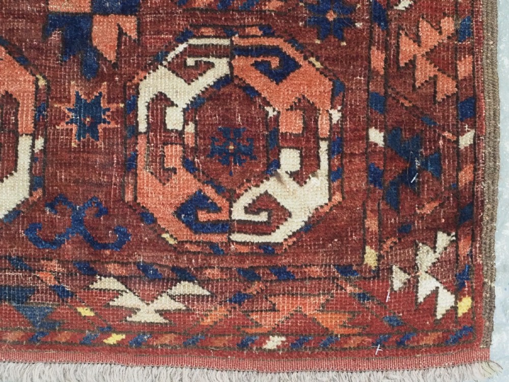 An antique woven wool rug featuring repeated octagonal gol motifs in cream, navy, and terracotta against a rich reddish-brown ground. View XI