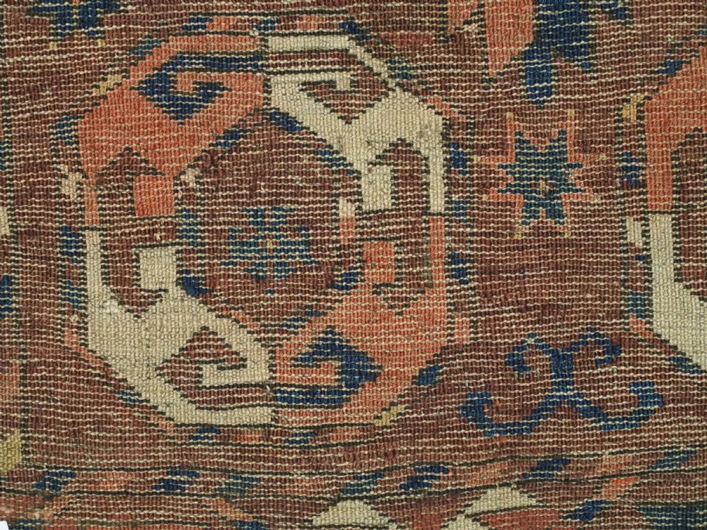 An antique woven wool rug featuring repeated octagonal gol motifs in cream, navy, and terracotta against a rich reddish-brown ground. View XII