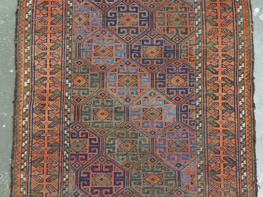 An antique Afghan Baluch wool rug featuring a repeating geometric hexagonal lattice pattern in terracotta orange, navy blue, sky blue, and sage green. View III