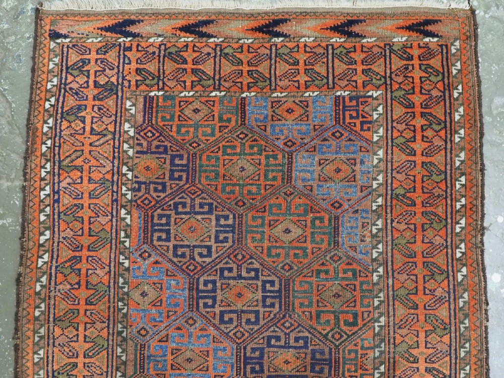 An antique Afghan Baluch wool rug featuring a repeating geometric hexagonal lattice pattern in terracotta orange, navy blue, sky blue, and sage green. View IV