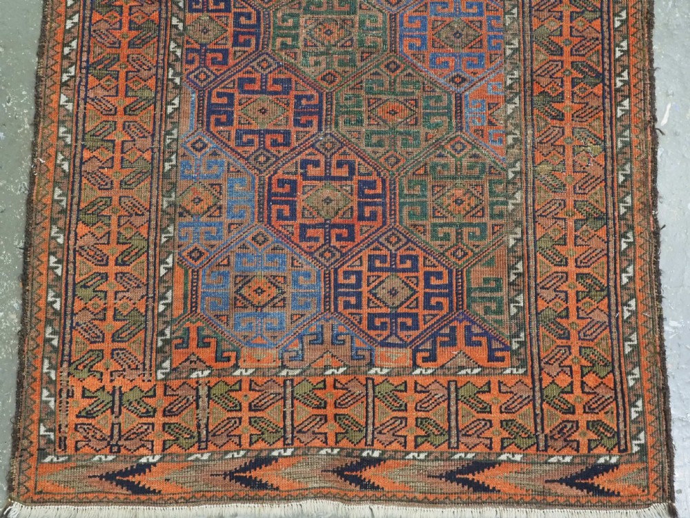 An antique Afghan Baluch wool rug featuring a repeating geometric hexagonal lattice pattern in terracotta orange, navy blue, sky blue, and sage green. View V