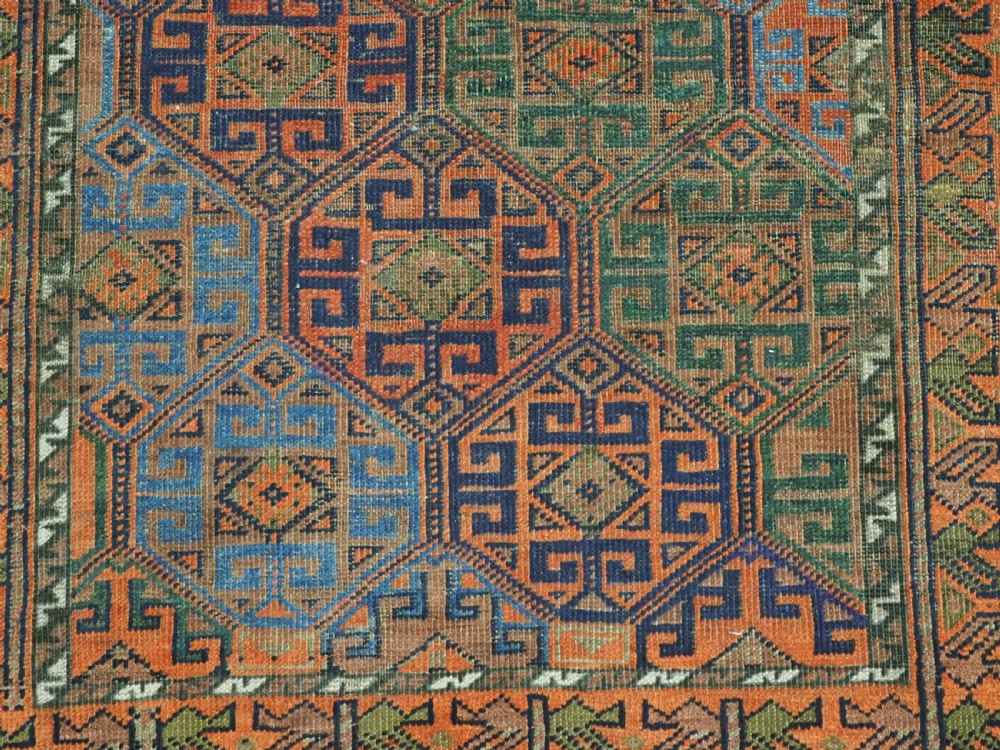 An antique Afghan Baluch wool rug featuring a repeating geometric hexagonal lattice pattern in terracotta orange, navy blue, sky blue, and sage green. View X
