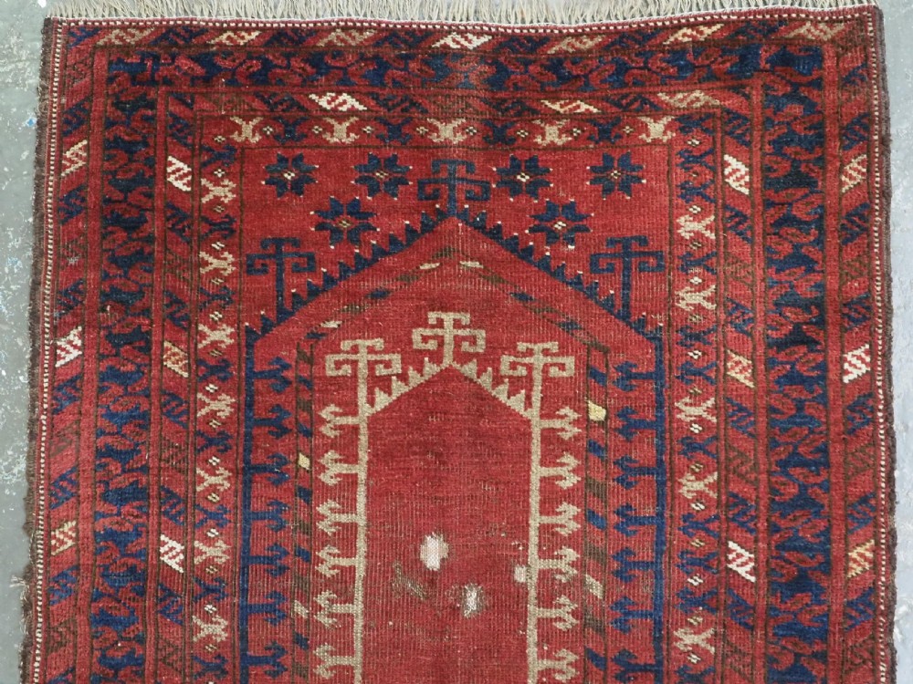 An antique hand-knotted Turkmen prayer rug featuring a red field with a central stepped arch motif and dark blue geometric borders. View III