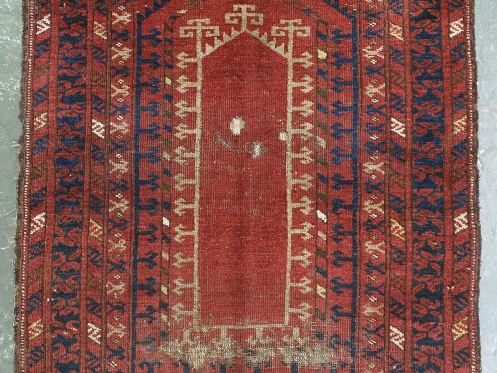An antique hand-knotted Turkmen prayer rug featuring a red field with a central stepped arch motif and dark blue geometric borders. View IV
