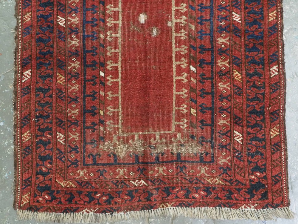 An antique hand-knotted Turkmen prayer rug featuring a red field with a central stepped arch motif and dark blue geometric borders. View V