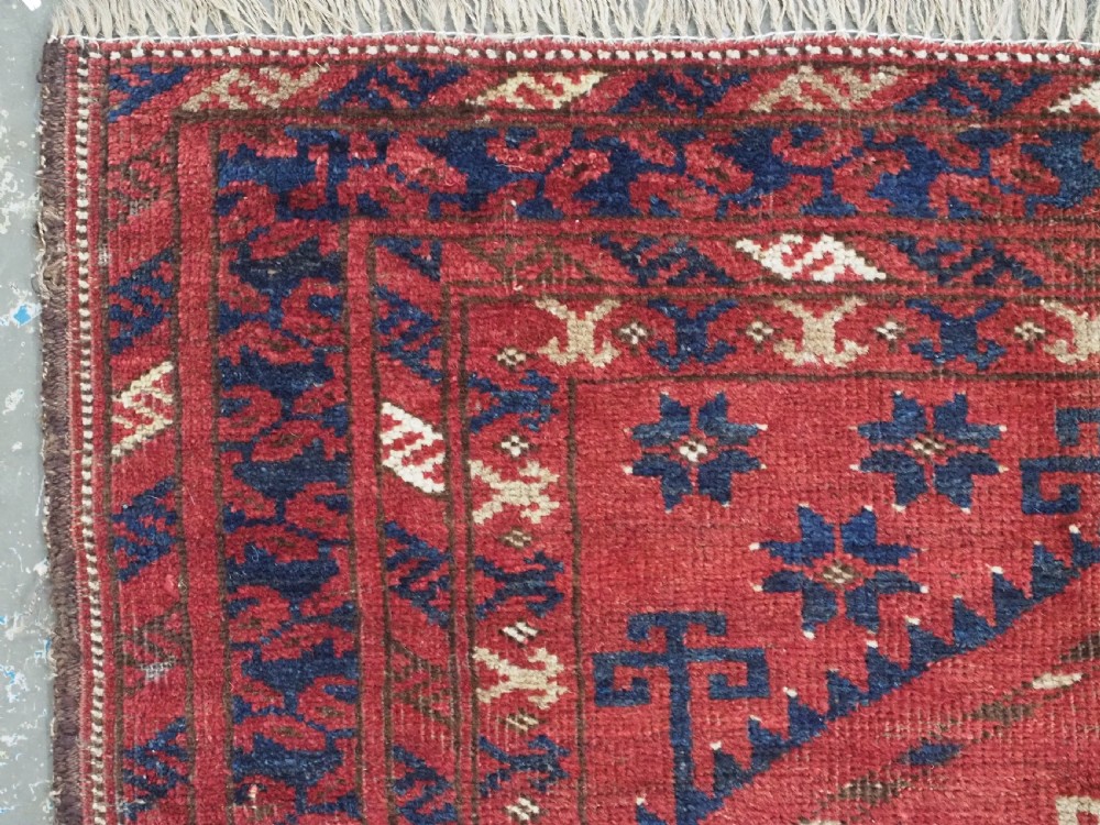 An antique hand-knotted Turkmen prayer rug featuring a red field with a central stepped arch motif and dark blue geometric borders. View VI