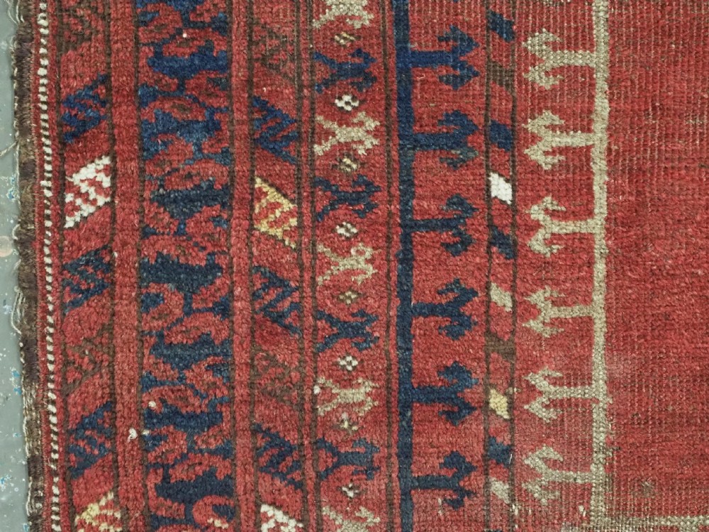 An antique hand-knotted Turkmen prayer rug featuring a red field with a central stepped arch motif and dark blue geometric borders. View VII
