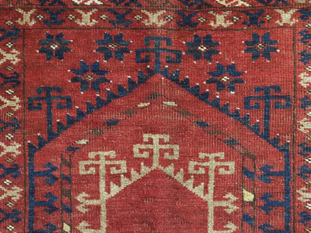 An antique hand-knotted Turkmen prayer rug featuring a red field with a central stepped arch motif and dark blue geometric borders. View VIII
