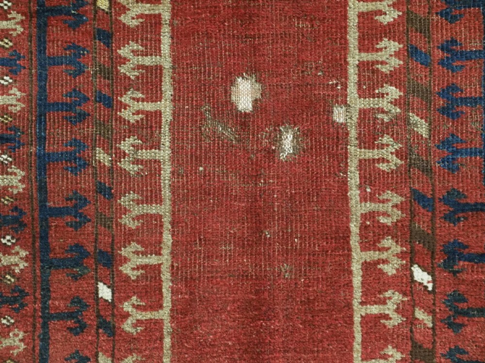 An antique hand-knotted Turkmen prayer rug featuring a red field with a central stepped arch motif and dark blue geometric borders. View IX