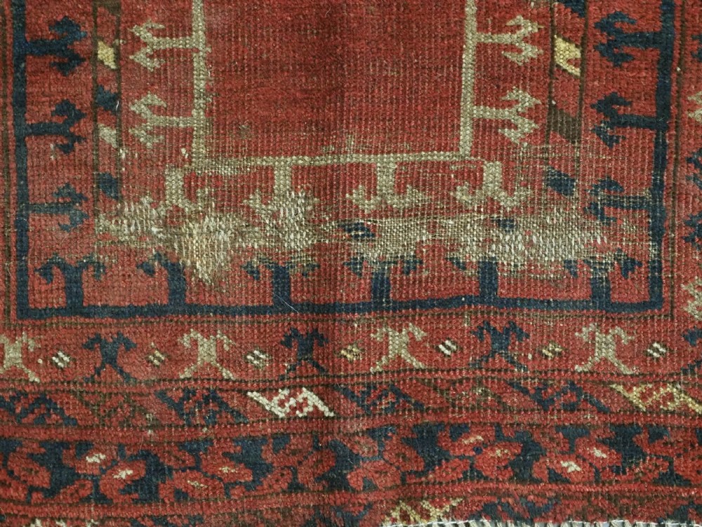 An antique hand-knotted Turkmen prayer rug featuring a red field with a central stepped arch motif and dark blue geometric borders. View X
