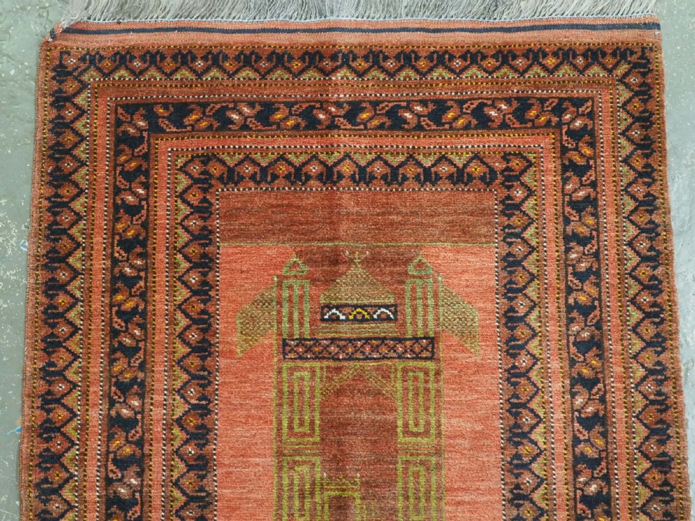 An antique hand-knotted Afghan Turkmen prayer rug featuring a central arch motif on a terracotta wool field framed by dark navy geometric borders. View III