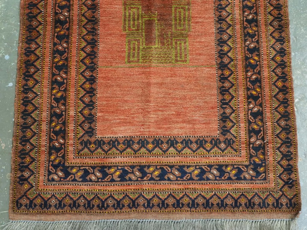 An antique hand-knotted Afghan Turkmen prayer rug featuring a central arch motif on a terracotta wool field framed by dark navy geometric borders. View IV